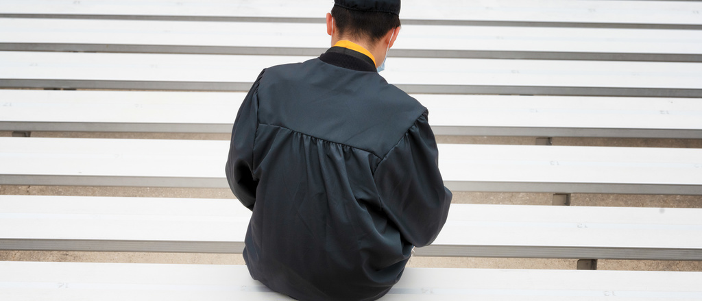 Person sitting on bleachers in graduation regalia